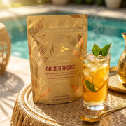Golden Tropic tea package on a sunny tropical patio beside iced tea